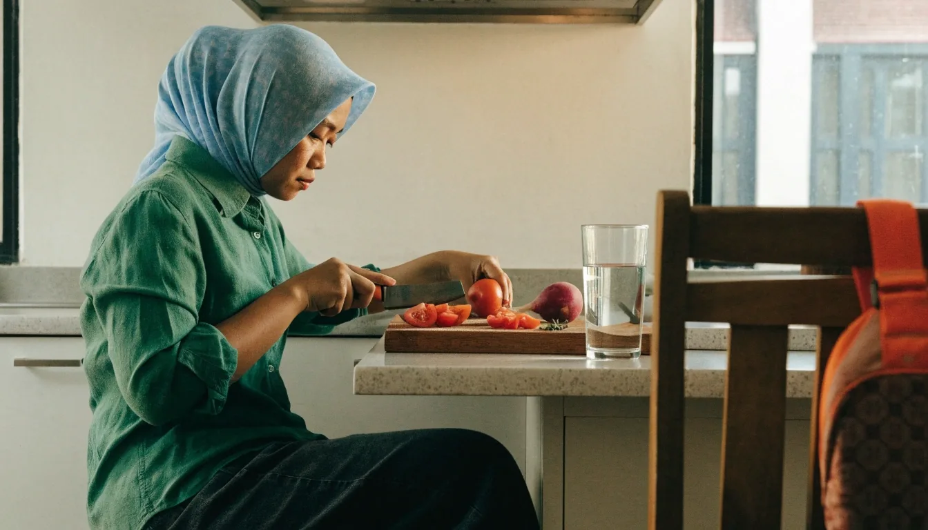 Hands breaking apart a piece of sliced pomelo above a matte stone plate on a low counter, soft shoji light from the upper left
